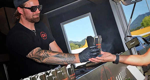 Mann gibt Essen aus einem Foodtruck - Gourmet Kartell